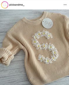 a knitted sweater with daisies on it and a name tag attached to the front