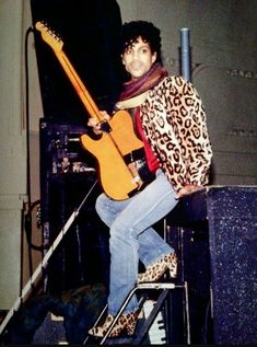 a man sitting on top of a chair with a guitar in his hand and an animal print jacket