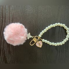 a pink pom - pom is attached to a white beaded bracelet with a heart charm