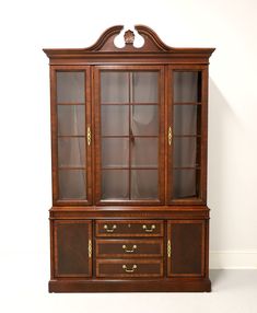 an antique china cabinet with glass doors and drawers on the front, against a white wall