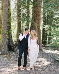 a bride and groom walking through the woods