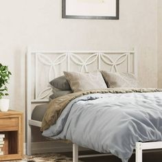 a white bed sitting next to a nightstand with a potted plant on top of it