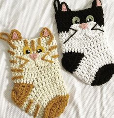 two crocheted cats sitting next to each other on top of a white sheet