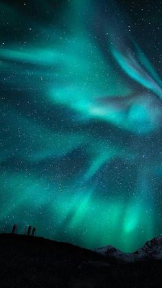 the sky is filled with green and blue aurora bores as people stand on top of a hill