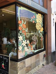 there is a window decorated with flowers in the storefront and sign on the sidewalk