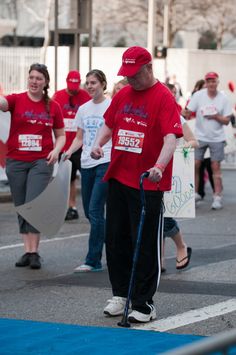 a man with a cane walking down the street in front of other people wearing red shirts