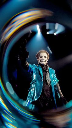 a man in a blue jacket and mask on stage with his hand up to the sky