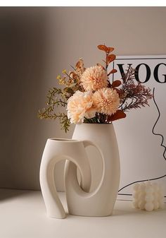 a white vase with flowers in it sitting on a table next to a candle holder