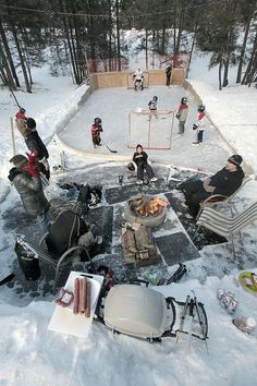 a group of people sitting around a fire pit on top of snow covered ground next to trees