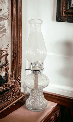 a large glass vase sitting on top of a wooden table next to a framed mirror