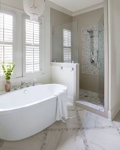 a white bath tub sitting in a bathroom next to a window filled with shutters