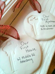 two white cookies with red ribbon on top of each one and the words our first house are written on them