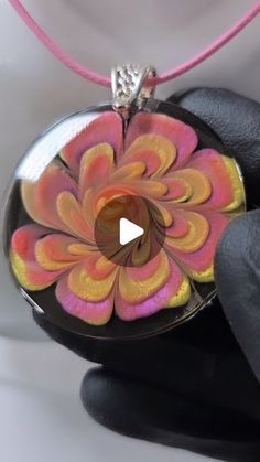 a hand holding a glass pendant with an orange and pink flower