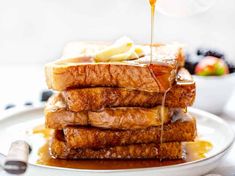 a stack of french toast with syrup being drizzled over it on a white plate