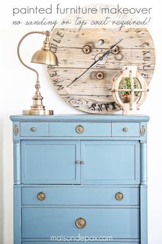 a blue dresser with an old clock on it's face next to a lamp