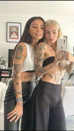 two beautiful women standing next to each other in front of a mirror with tattoos on their arms