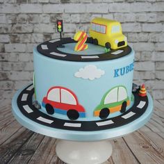 a blue cake with cars on it sitting on a table next to a brick wall