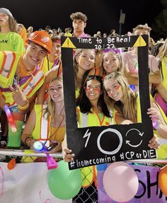 a group of young people standing next to each other in front of a fence with balloons