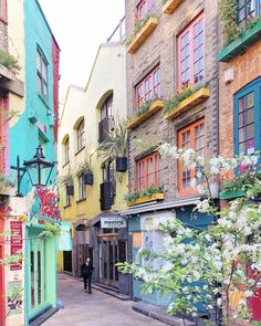 a person walking down an alley way in front of some buildings with flowers on the windows