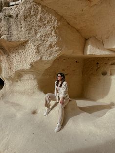 a woman sitting on the ground in front of a rock formation with her legs crossed