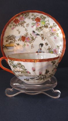 an old china tea cup and saucer with floral designs on the rim, sitting on a stand