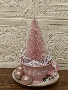 a pink christmas tree sitting in a cup on top of a saucer filled with candy