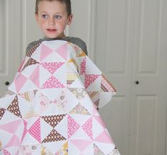 a young boy is holding up a quilt made from triangle shapes and triangles on it