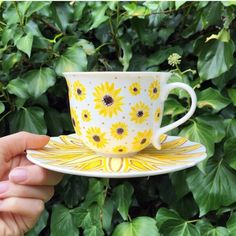 a hand holding up a yellow and white tea cup on top of a saucer