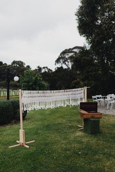 an outdoor ceremony setup with white chairs and lace curtains on the grass, in front of a row of trees