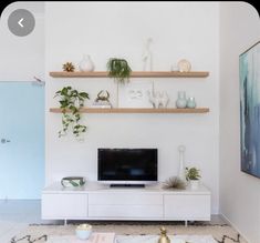 a living room with white walls and shelves on the wall, plants in vases