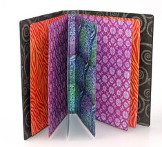 an open book with colorful designs on the pages and inside is black, orange, purple, and pink