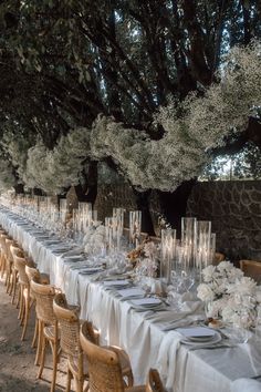 a long table is set up with white flowers and place settings for an outdoor dinner