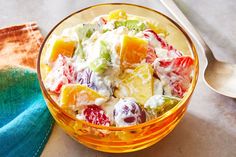 a glass bowl filled with fruit salad on top of a table next to a spoon