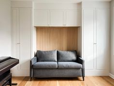 a grey couch sitting in front of a wooden shelf next to a black tv on top of a hard wood floor