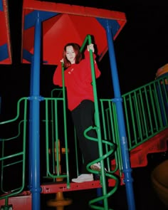 a woman standing on top of a blue and green playground structure at night with an umbrella over her head