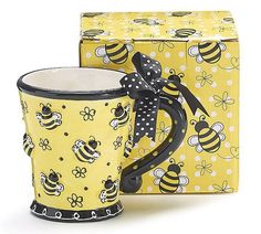 a yellow and black coffee mug next to a box with a bee design on it