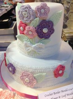 a three tiered cake with crocheted flowers on it's sides and ribbons around the edges