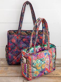 two purses sitting next to each other on top of a wooden table with white wall behind them