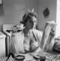 a woman sitting at a table with a cup and newspaper in her hand while reading the paper