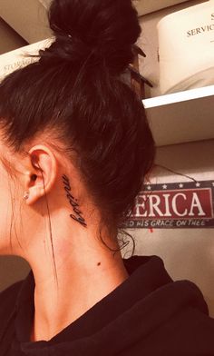 a woman with a tattoo on her neck and behind her ear stands in front of shelves