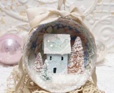 a glass ornament with a small house in the middle and trees on it