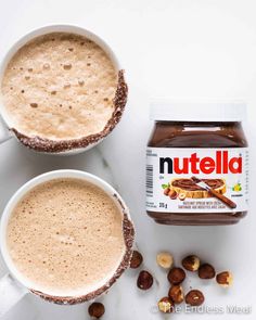 two mugs filled with nutella next to nuts on a white counter top,