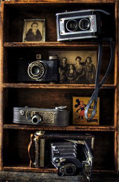 an old wooden bookcase filled with antique cameras and other items on top of it