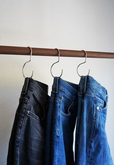 three pairs of jeans hanging on a wooden rail