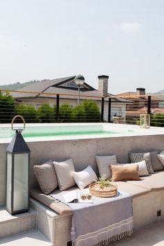 a couch sitting on top of a patio next to a table with pillows and a lantern