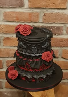 a black hat with red roses on it sitting next to a brick wall in front of a wooden table