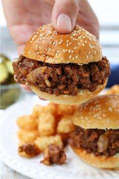 a person is holding up a hamburger with meat on it and french fries in the background