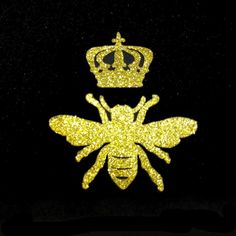 a gold glitter bee with a crown on it's head, sitting next to a black background