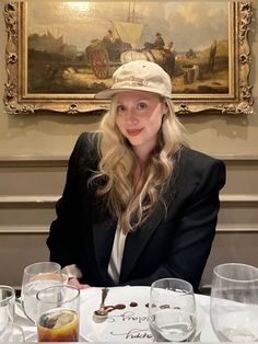 a woman sitting at a table in front of a painting with glasses on the table