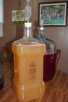 a bottle of liquid sitting on top of a wooden table next to a glass jug